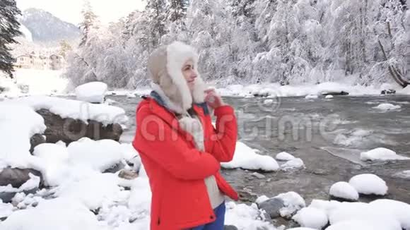 一个穿着红色夹克衫的女人在冬天的河边享受着一个寒冷的早晨把雪扔在身上旋转着视频的预览图