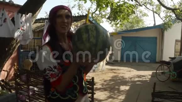 穿着乌克兰民间服装的女孩手里拿着西瓜在一个农村院子里晒衣服的背景上摆着相机视频的预览图
