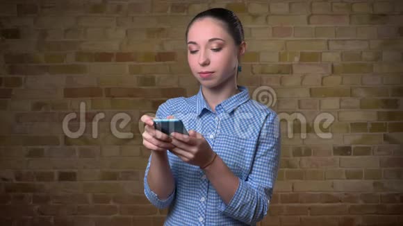 白种人女人的肖像马尾辫专注地看着智能手机上的布里肯墙背景视频的预览图