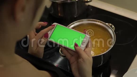 一位女士拿着一部绿色屏幕的智能手机正在煮汤视频的预览图