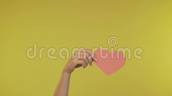 雌性的手在一个孤立的黄色背景上抛出一张大心脏的纸4K视频的预览图