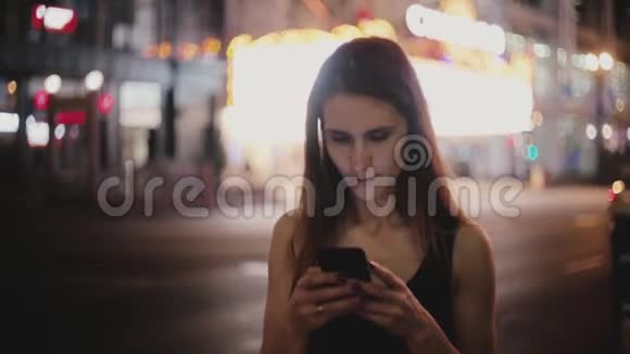 大气中拍摄的快乐白种人年轻当地妇女使用智能手机应用程序在黑暗的纽约夜街微笑视频的预览图