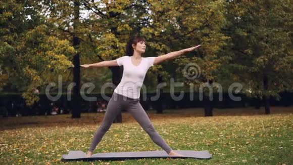迷人的年轻女子正在户外做瑜伽站在垫子上练习一系列的体式顺序视频的预览图