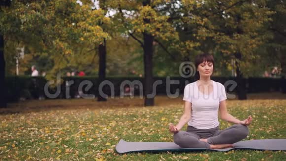 有魅力的年轻女士坐在公园里的瑜伽垫上双手抱在泥里跪着呼吸视频的预览图