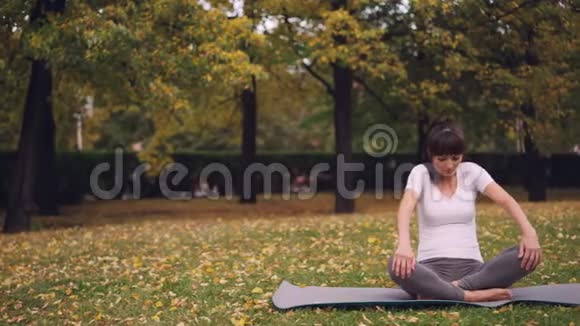 灵活的年轻女士为健康的脊柱做运动坐在瑜伽垫上在个人的时候向后移动视频的预览图