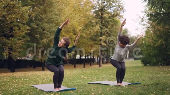 灵活的女孩正在练习椅子姿势站在公园的瑜伽垫上移动身体和头部美丽的秋天视频的预览图