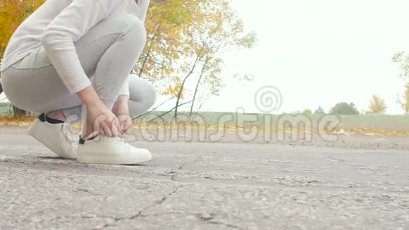 在秋天的大自然中在沥青跑道上系鞋带的跑步者年轻的女人准备开始跑步女孩从事户外运动视频的预览图