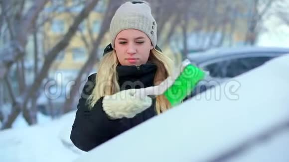 一个年轻的女孩用她的车刷从雪中清洁绿色冬天的早晨视频的预览图