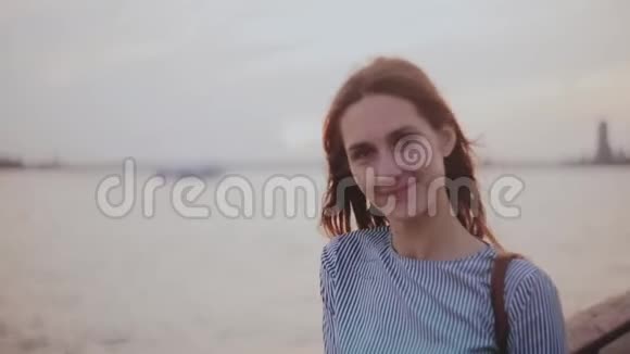 快乐年轻的欧洲女孩摆姿势的肖像看着相机头发在夕阳河滩的风中飘扬视频的预览图