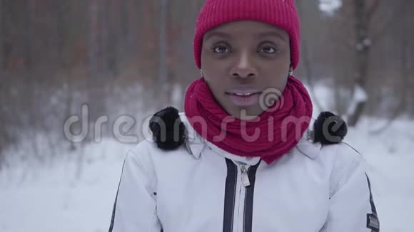 美国黑人女孩站在冬天的森林里看镜头特写的肖像穿暖和夹克的漂亮女孩视频的预览图
