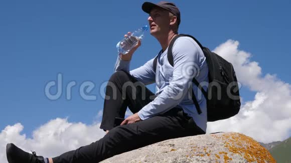 人坐在大石头上在徒步旅行的山上喝着瓶子里的水视频的预览图