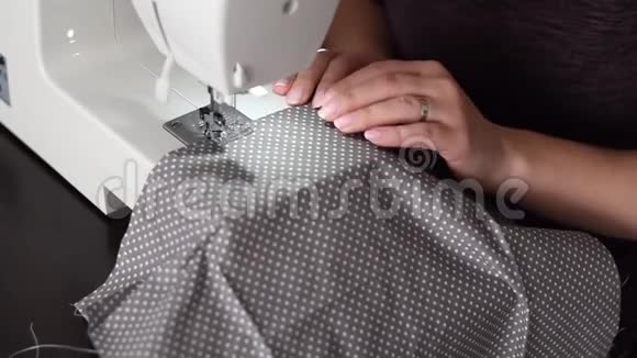 特写一位年轻女子用缝纫机缝制一件灰色白点棉布的镜头录像视频的预览图