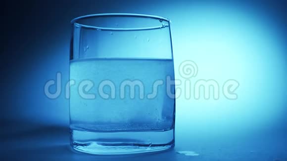 阿司匹林或泡腾药丸在蓝色背景下缓慢滴入一杯水中视频的预览图