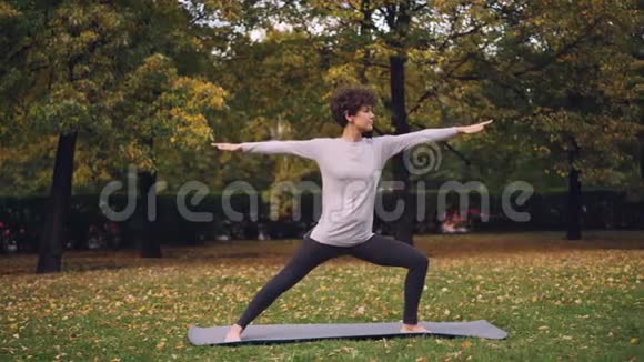 留着短卷发的漂亮女孩正在户外做瑜伽站在勇士的姿势下伸展身体和腿部视频的预览图