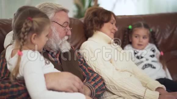 快乐的白发苍苍的祖父和可爱的祖母拥抱和交谈他们的小有趣的孙女视频的预览图