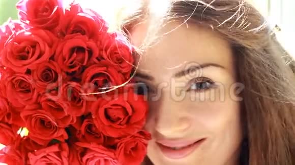 美丽的女人特写微笑着嗅着红玫瑰花的香气头发女孩的风视频的预览图