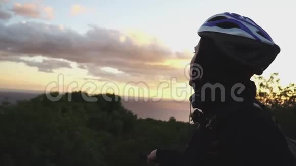 骑自行车的女孩站在路上欣赏日落时的海景视频的预览图