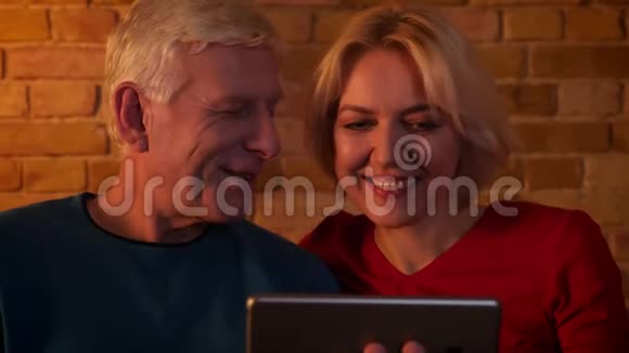 在一间舒适的公寓里坐在沙发上的一对老年幸福夫妇在平板电脑上视频通话的特写镜头视频的预览图