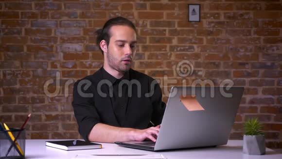白人商人坐在砖砌的办公室里双手放在电脑后面视频的预览图