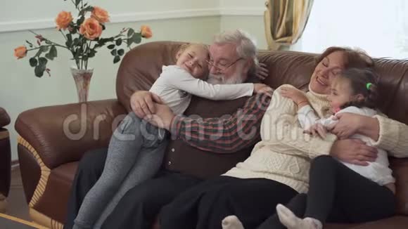 祖父和祖母坐在现代客厅的皮沙发上旁边有两个小女孩孙女视频的预览图