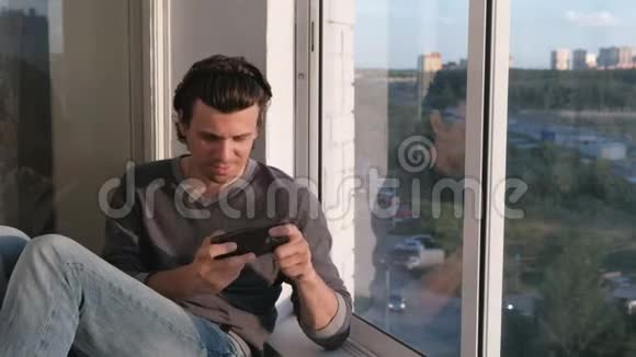 日落时分男人坐在阳台上玩手机游戏视频的预览图