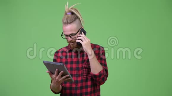 快乐的留着胡子的嬉皮士男人在使用数码平板电脑的时候用电话说话视频的预览图