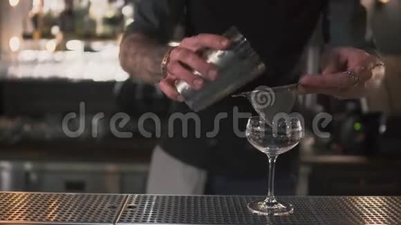 酒吧柜台上的酒吧服务员用高玻璃筛把粉红色牛奶鸡尾酒倒入男人动作非常视频的预览图