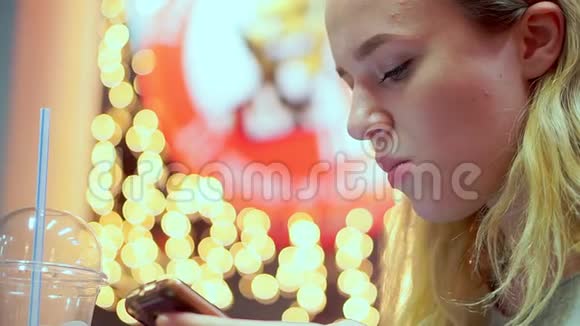 年轻的少女读智能手机信息她正在咖啡馆里吃晚饭快餐晚上在灯光的背景下视频的预览图
