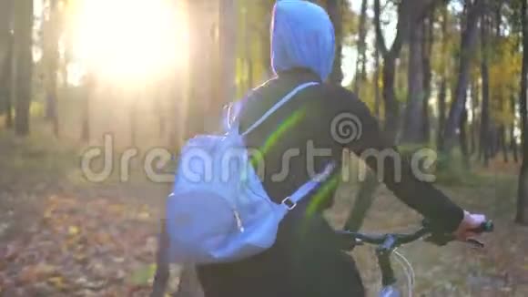 戴着头巾背着背包的穆斯林妇女在秋季公园骑自行车视频的预览图