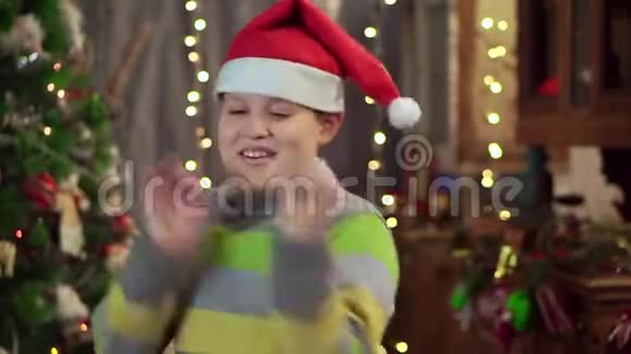 一个戴着帽子的少年圣诞老人正在圣诞树附近跳舞圣诞假期新年快乐视频的预览图