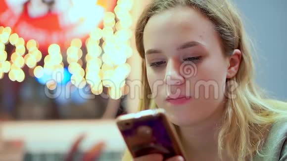 年轻的少女读智能手机信息她正在咖啡馆里吃晚饭快餐晚上在灯光的背景下视频的预览图