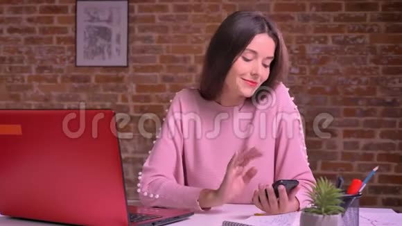 快乐的年轻女性在工作场所用红色笔记本电脑在砖背景前刷卡视频的预览图