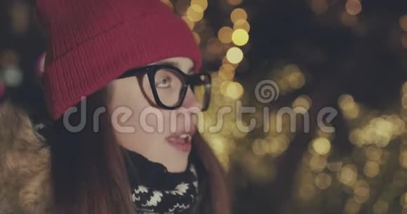 在夜晚模糊的圣诞灯光下幸福的女孩看着一件令人陶醉的事情视频的预览图