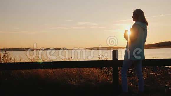 孤独的女人在湖边喝啤酒独自站在篱笆旁看着夕阳视频的预览图