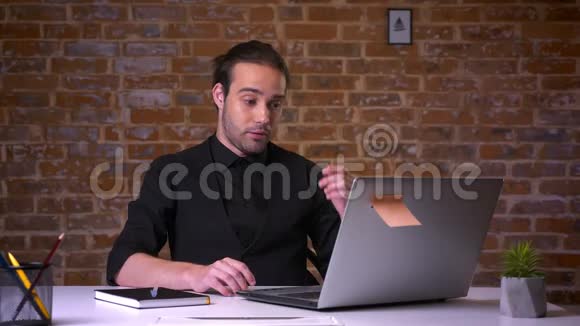 失望的白种人男性穿着黑色西装双手看着笔记本电脑坐在砖墙附近视频的预览图