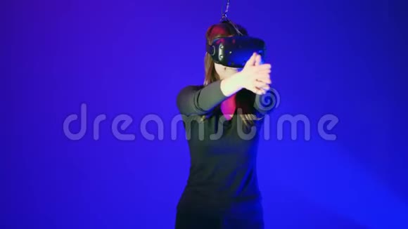 年轻女子在VR耳机玩得开心玩互动电子游戏蓝色背景下的虚拟现实头盔视频的预览图