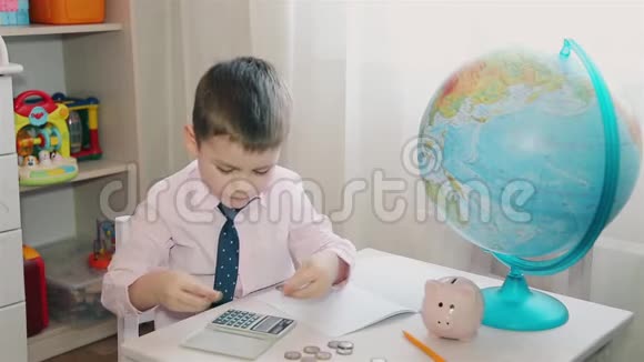 一个小男孩把他的积蓄记在计算器上然后把钱记在笔记本上视频的预览图