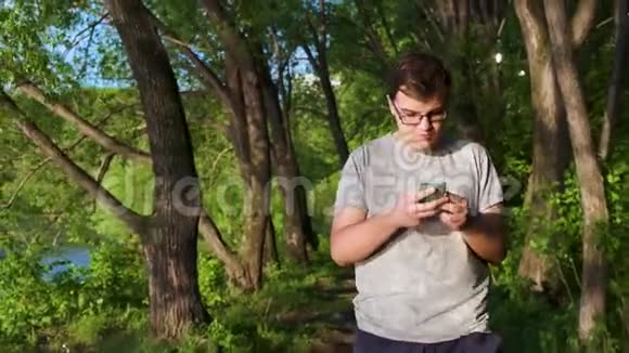 年轻人手里拿着手机在森林里探险时发短信库存录像男性视频的预览图
