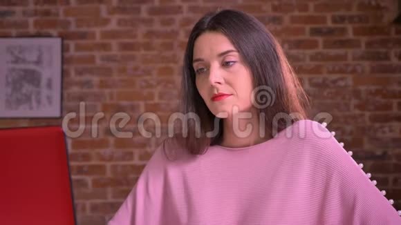 漂亮的高加索商务女性坐在桌旁的粉红色套头衫上努力工作打着哈欠视频的预览图