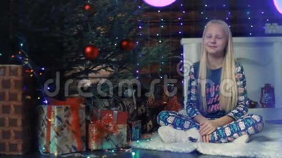 一个留着长发的小女孩坐在圣诞树下微笑着视频的预览图