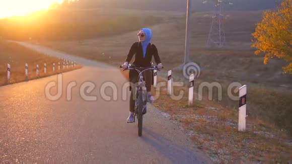 穆斯林妇女戴头巾背着背包骑着自行车在路上夕阳西下慢悠悠视频的预览图