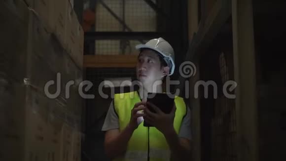 年轻的仓库工人戴着安全安全帽带着数字平板电脑穿过库存室视频的预览图