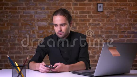 穿着黑色西装严肃的白种人男性双手拿着电话坐在办公桌前思考并专注于自己的思想视频的预览图