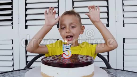 可爱的五岁男孩穿着t恤庆祝他的生日在自制的烤芝士蛋糕上吹蜡烛室内视频的预览图
