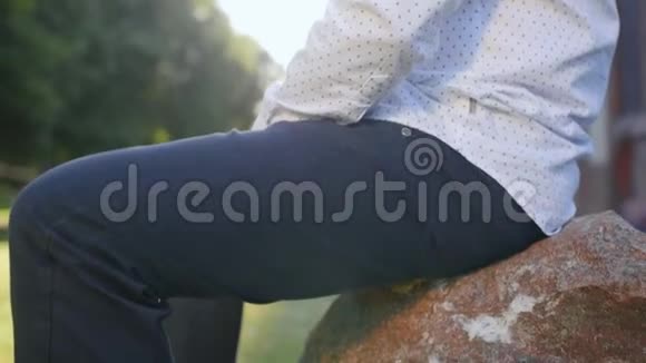 穿着经典衬衫的人走近石头坐在公园里视频的预览图