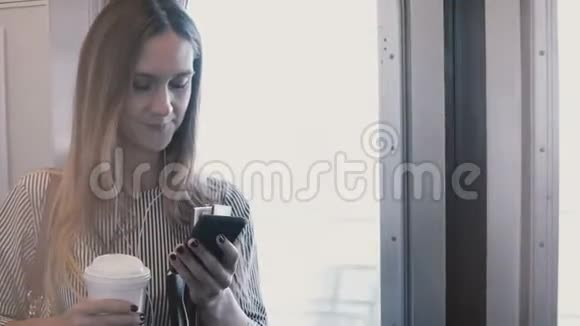快乐轻松美丽的女学生在地铁列车上看智能手机使用信使微笑与咖啡杯视频的预览图