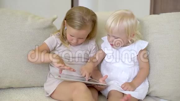 两个孩子在家用平板电脑看ang儿童使用现代笔记本电脑平板电脑在沙发上小女孩在玩视频的预览图