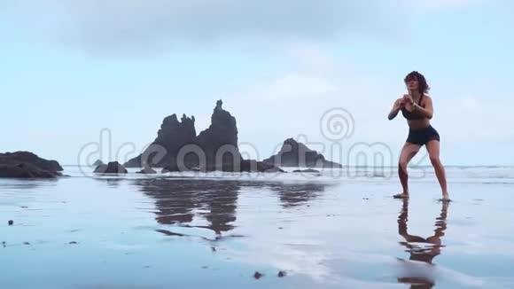 女孩在海滩上蹲着训练后跳了出来在大西洋附近有黑色的沙子视频的预览图