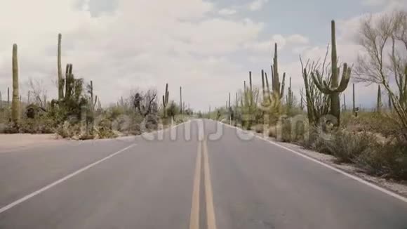 相机迅速倾斜在空旷的沙漠道路中间大萨瓜罗仙人掌生长在美国亚利桑那州的两侧视频的预览图