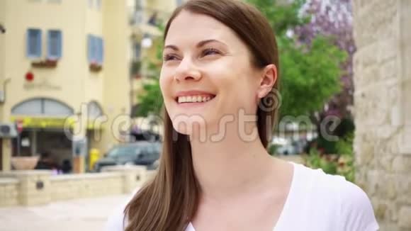 穿着白色t恤微笑的年轻女子慢悠悠地走在欧洲城市的大街上四处张望视频的预览图